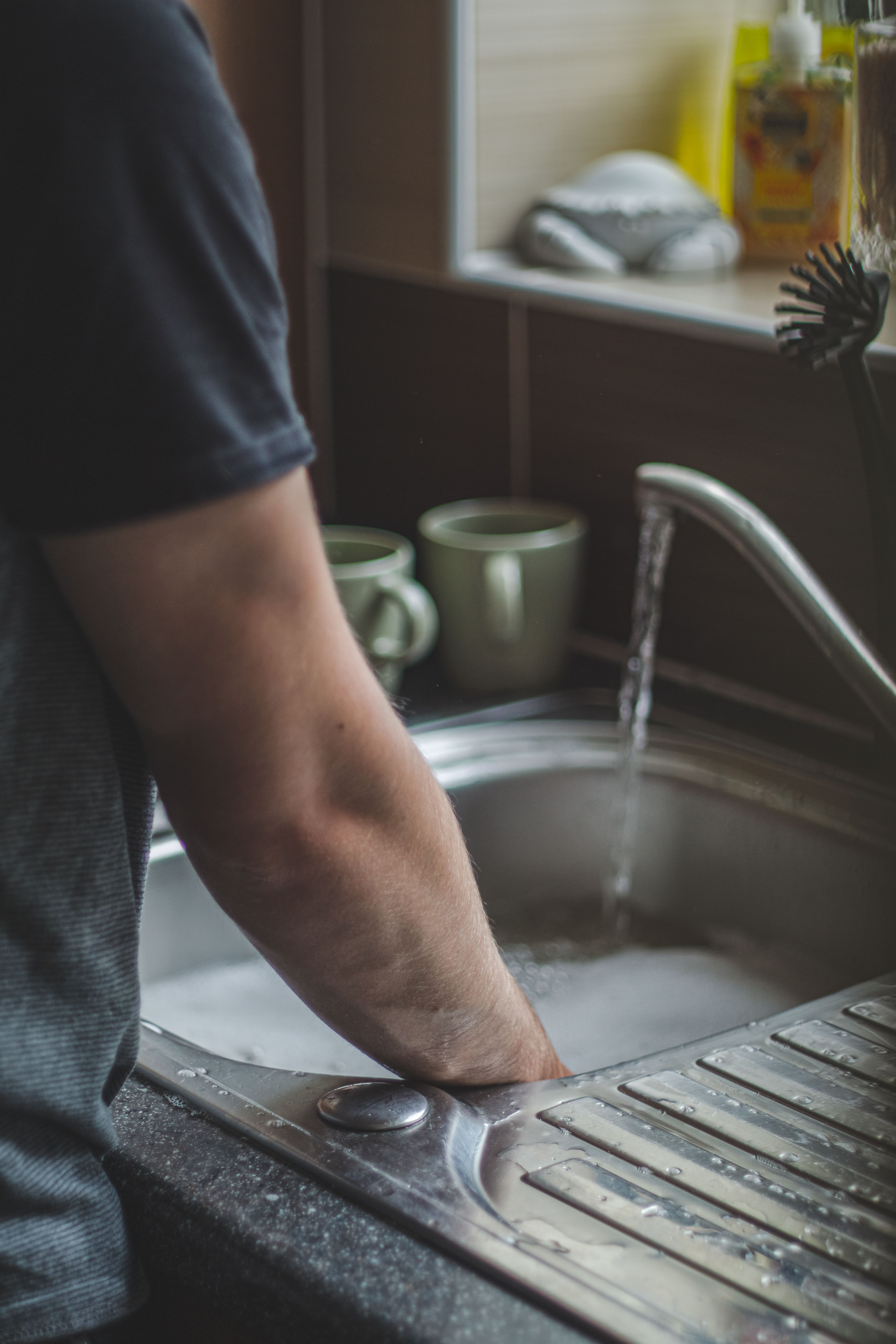 Hands being washed beneath a running kitchen tap.