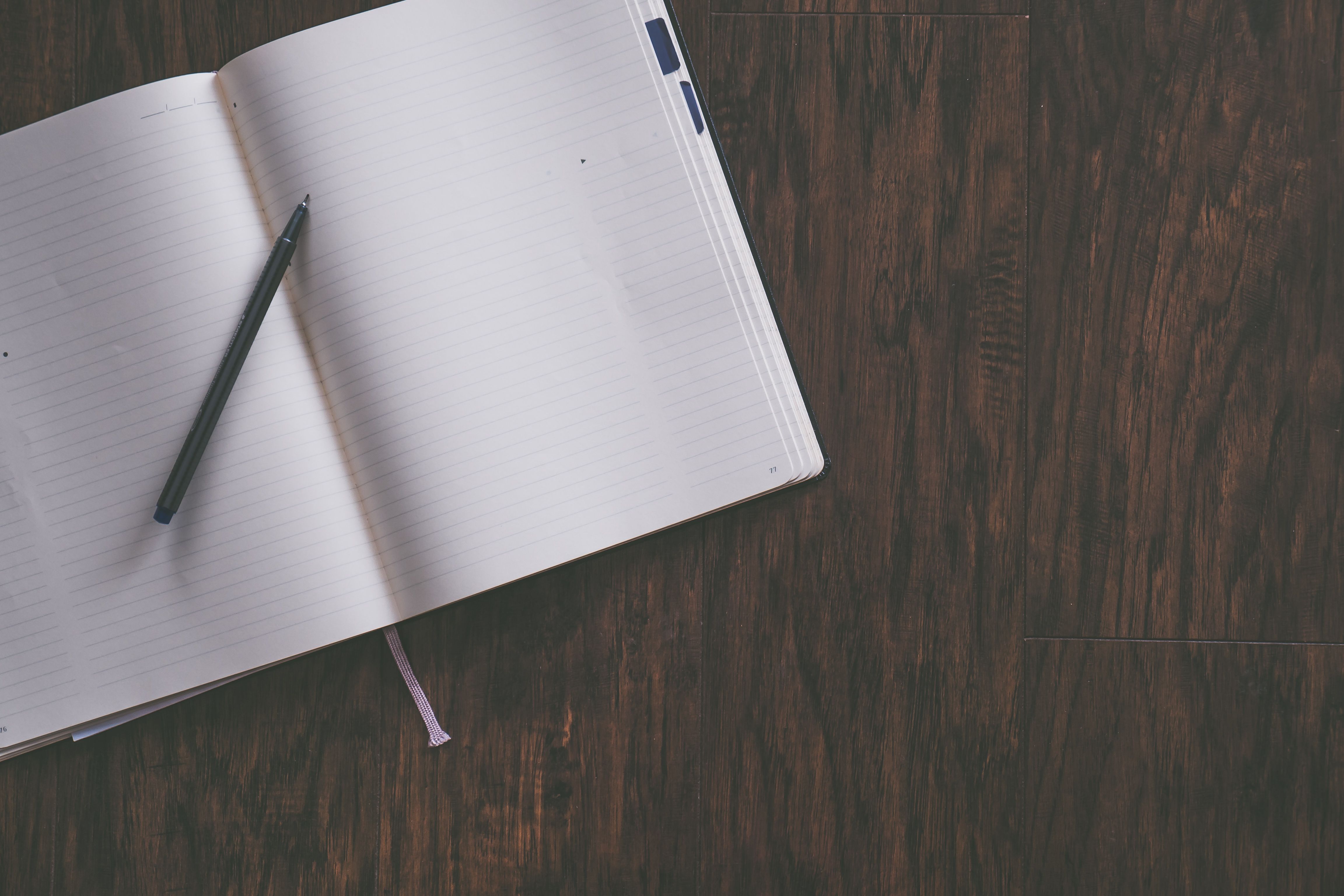 An open notebook and pen on a wooden desk.